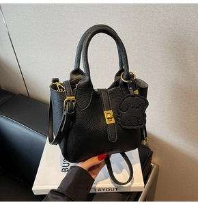 Detail of black lychee grain leather bucket bag with gold hardware and puppy charm
