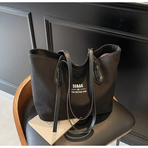 Detail of black canvas tote bag with white text logo and sleek leather shoulder straps