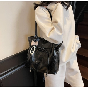 Dettaglio della borsa tote in vernice nera con coulisse e ciondolo con perle