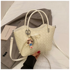 Detail of cream woven bucket bag with metal handle, ribbon bow, and cartoon charm