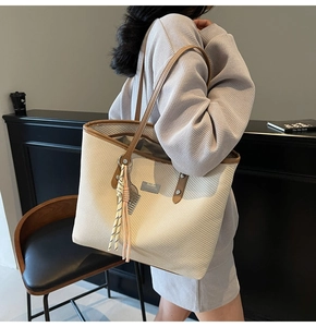 Detail of woven tote bag with brown leather straps and decorative tassel charm