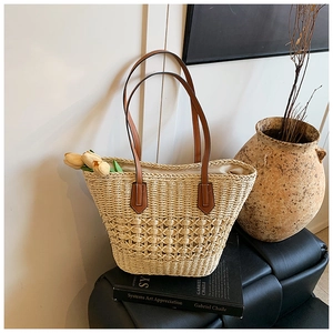 Detail of hand-woven straw tote with premium brown leather handles and reinforced patches