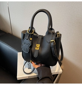 Detail of black lychee grain leather bucket bag with gold lock and dog charm