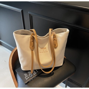 Detail of a large canvas tote bag with brown leather handles on a dark leather chair