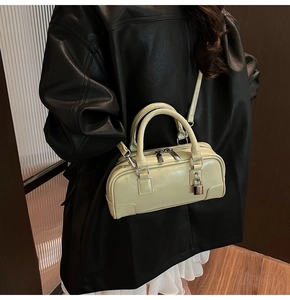 Close-up of light green Boston bag featuring glossy leather and silver lock on black leather jacket