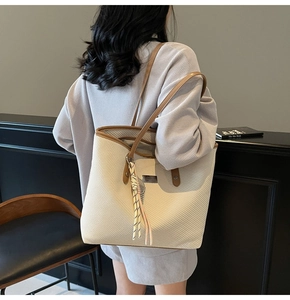 Detail of a large beige woven tote bag with brown leather straps and metal logo plate