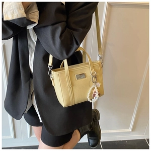 Detail of beige lychee leather crossbody bucket bag with pearl and doll pendant on a model