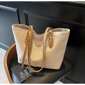 Close-up of beige canvas tote bag with brown leather straps on a modern chair