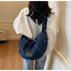 Detail of a large dark blue denim crescent bag with adjustable strap on a model