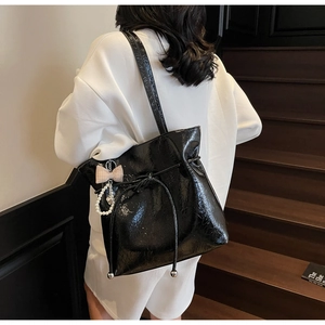 Détail du sac cabas en cuir verni noir avec cordon de serrage, nœud et perles nacrées