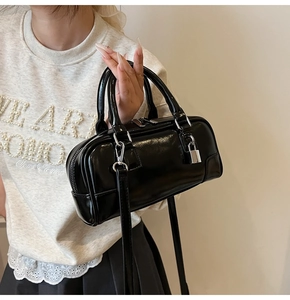 Detail shot of a black patent leather Boston bag with silver zipper and mini padlock charm
