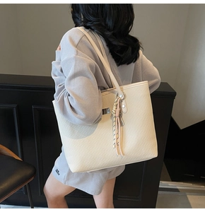 Detail view of cream tote bag with diagonal woven texture and striped tassel charm