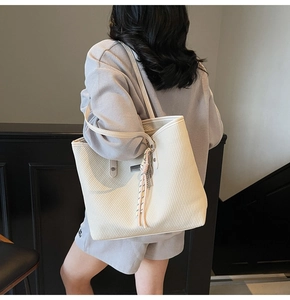 Detailed view of beige tote bag featuring textured diagonal pattern and tassel charm