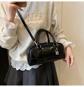Detail of a black shiny Boston bag with silver lock and detachable shoulder strap