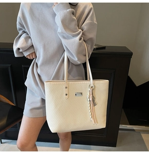 Detail shot of cream tote bag with woven texture and silver rectangle metal logo