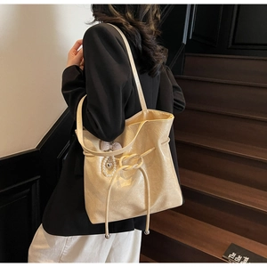Dettaglio di una borsa tote beige crema lucida con ciondolo a perla e texture morbida