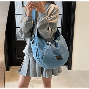 Macro shot of light blue denim crossbody bag featuring floral knot and brand label