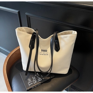 Detail of off-white canvas tote bag featuring black SOBAG lettering and leather handles