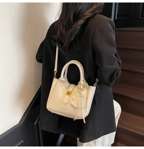 Close-up of cream leather bucket bag with pebble grain and gold lock on stairs
