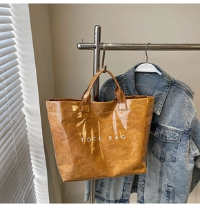 Braune Shopper-Tasche aus Dupont-Papier mit TOTE BAG Aufdruck neben Denim-Jacke