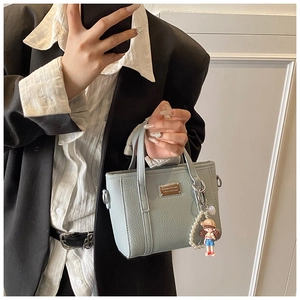 Detail of light blue pebble leather handbag with metal logo and pearl doll charm