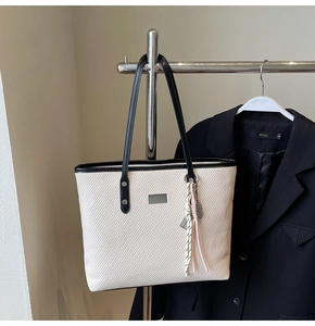 Detail of cream woven tote bag with black leather trim and silver brand tag hanging on rack