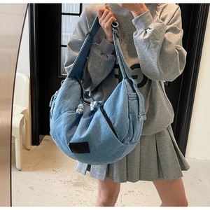 Detail of light blue denim crossbody bag with frayed edges and adjustable wide strap