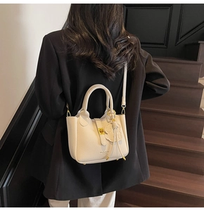 Detail of cream lychee leather bucket bag with gold lock and bear pendant on black blazer