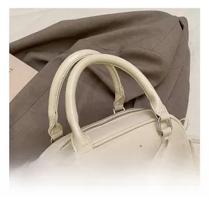 Detail shot of a cream leather handbag with double handles and metal logo plate