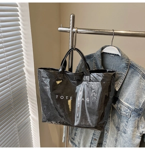 Detail der glänzenden schwarzen Tote Bag mit weißem Aufdruck neben einer Jeansjacke