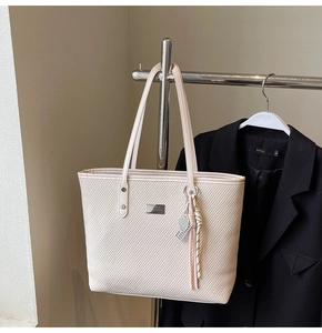 Detail of cream tote bag texture with silver logo and tennis racket charm accessory