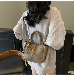 Detail of taupe pebbled leather bucket bag featuring gold hardware and a cute bear charm