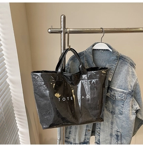 Borsa tote nera lucida con scritta TOTE BAG bianca appesa a un supporto per uso quotidiano