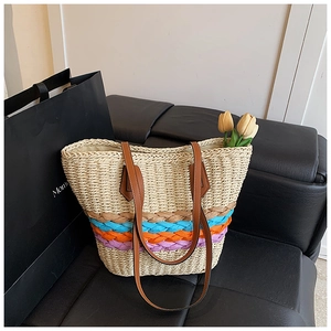 Détail du sac cabas en paille à rayures colorées et bandoulière en cuir sur un canapé