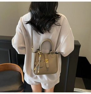 Taupe pebbled leather bucket bag with top handle and gold clasp shown on model