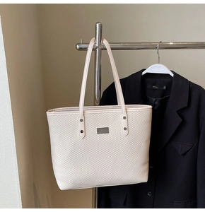 Detail of beige tote bag showing twill woven texture and rectangular metal logo tag