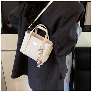Detail of beige lychee grain leather mini tote bag with a cute pearl doll charm on side