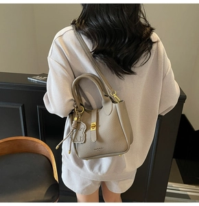 Detail showing taupe lychee leather texture with gold buckle and cute bear charm