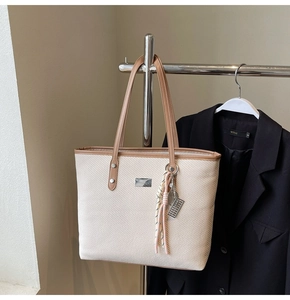 Detail of cream woven tote bag with brown leather straps and metal abacus charm