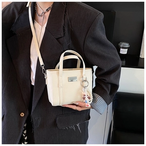 Detail of cream grained leather mini tote bag with pearl charm and silver logo plaque