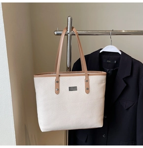 Close-up of beige woven texture tote bag with brown leather straps and metal rivets