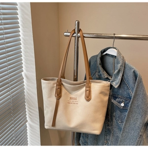 Detail of off-white canvas tote bag featuring brown leather handles and SOBAG lettering