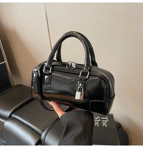 Detail of black patent leather Boston bag with silver padlock and double zipper closure