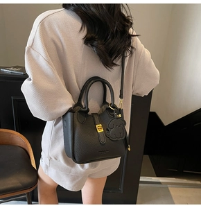 Detail of black pebbled leather bucket bag featuring gold twist lock and cute dog charm