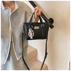 Detail of black lychee leather crossbody bag with silver hardware and pearl doll charm