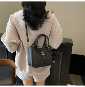 Detail of black pebbled leather bucket bag with gold clasp and dog charm on a model