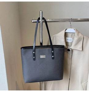 Detail of grey woven texture tote bag with black handles and silver metal nameplate
