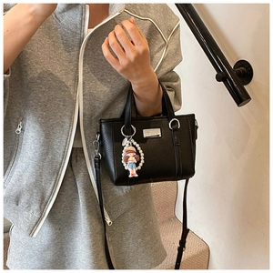 Detail of black lychee grain leather tote with silver logo and pearl doll charm