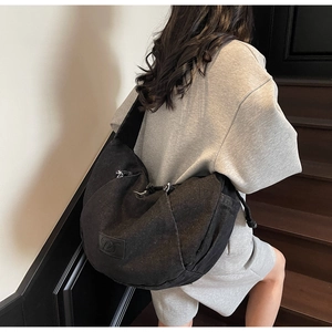 Detail of a black denim dumpling bag showing soft silhouette and wide shoulder strap