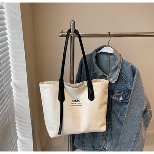 Detail of off-white canvas tote bag with black long straps and branded front text